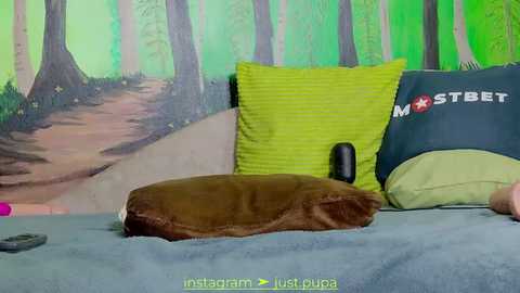 Media: Video of a cozy bedroom with a brown pillow and green blanket on a bed, featuring a wall mural of a forest path, and a \"MSTBET\" pillow.