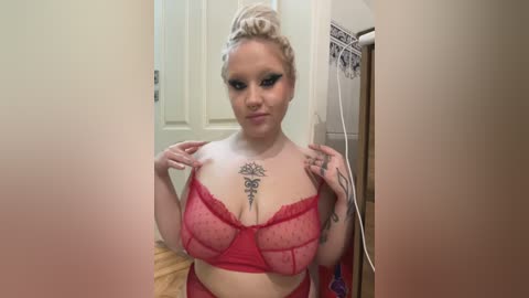 Media: A video of a curvy, fair-skinned woman with blonde hair in a bun, wearing a red lace bra and panties, with tattoos on her chest and arms, standing in a bathroom doorway.