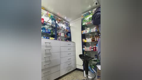 Media: Video of a small, well-lit medicine cabinet with white drawers and shelves filled with various medications, cosmetics, and personal care items.