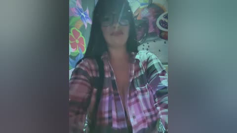 A blurry video of a young woman with long black hair, wearing glasses and a plaid shirt, standing against a colorful, floral-patterned backdrop.