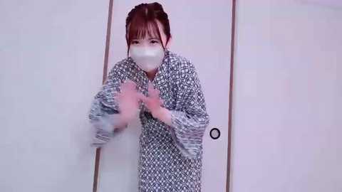 Media: A video of an Asian woman in a traditional Japanese kimono with a mask, hands raised in a defensive posture. She stands in a white-walled room with sliding doors.