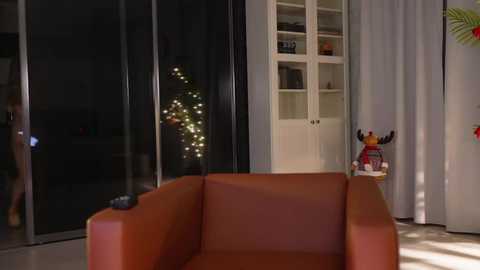 Media: Video of a modern living room with an orange sofa, white bookcase, and Christmas tree with fairy lights. A LEGO reindeer and a small Christmas tree are on the floor beside the sofa.