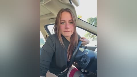 Media: A video of a fair-skinned, long-haired Caucasian woman in a black shirt, sitting in a car, with a blurred background of a suburban area.