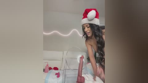 Media: A video of a woman in a red Santa hat, with long black hair, wearing a strapless outfit, smiling while using a large, realistic dildo.