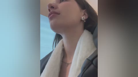 Media: Video of a woman with fair skin, dark hair, and light makeup, wearing a black coat with a white scarf, looking upward, in a dimly lit room.