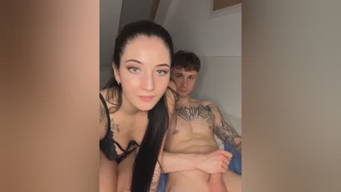 Media: Video of a topless, tattooed young man with a slender build and a woman with long black hair and a black bra, both smiling, in a dimly lit bedroom.