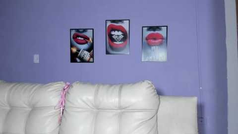 Media: Video of a living room wall with lavender paint, featuring three large, framed prints of red lips. A white leather sofa with a pink ribbon on the left.