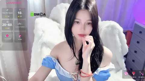 Media: A video of an East Asian woman with long black hair, wearing a blue off-shoulder top, lying on a white fur rug in a cozy room with purple lighting.