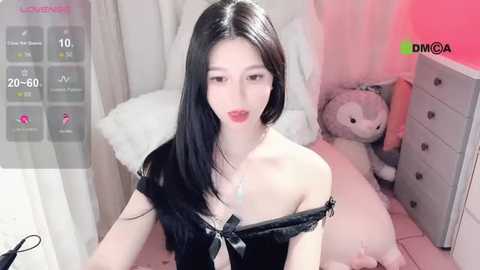 Media: Video of a slim Asian woman with long black hair, wearing a black off-shoulder top, in a pink-lit bedroom with plush toys and a dresser.