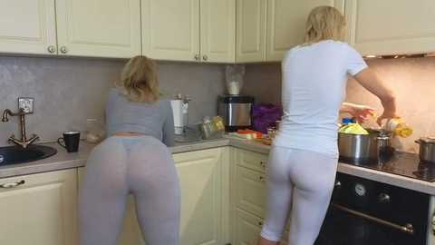 Media: Video of two blonde women in matching light blue pajamas standing in a modern kitchen. One is washing dishes, the other stirring a pot on the stove.