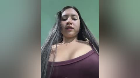 Media: Video of a young Latina woman with long, straight black hair, wearing a burgundy off-shoulder top, against a blurred green background.