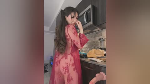 Media: Video of a woman with long dark hair in a sheer red lace robe, bending over in a modern kitchen with stainless steel appliances and a microwave.