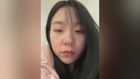 Media: A video of a young Asian woman with long black hair, wearing a pink jacket, looking somber, with blurred background.