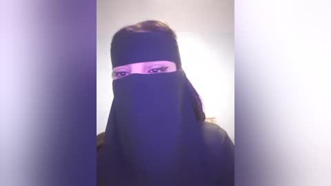 Media: A video of a person wearing a black niqab, with only their eyes visible, set against a plain white background, creating a dramatic, mysterious atmosphere.