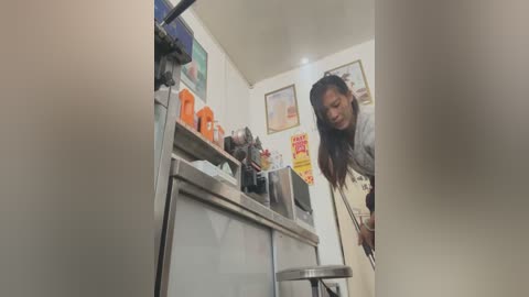 Media: A video of a woman with long hair, wearing a grey jacket, working behind a stainless-steel counter in a bright, minimalistic caf\u00e9.