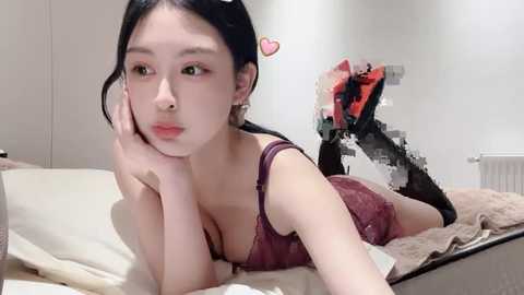 Media: A video of an Asian woman with pale skin and long black hair, lying on a bed in a white room, wearing a burgundy lace bra and black thigh-high stockings.