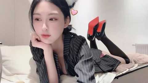 Media: Video of a young East Asian woman with pale skin, wearing black pinstripe pajamas, black thigh-high boots, and black cat ears, lying on a bed, looking seductively at the camera.