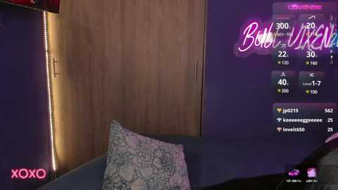 Media: A video of a modern bedroom with a plush gray pillow on a bed, a wooden wardrobe, purple wall, and a digital clock displaying 3:00 AM. The room's ambiance is cozy with soft lighting and a subtle pink 'XOXO' logo in the corner.