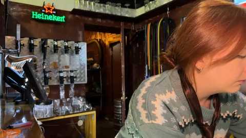 Media: Video of a dimly lit bar with a woman in a patterned shirt, glasses, and red hair, examining a glass rack.