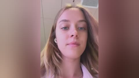 Media: A video of a young woman with fair skin, straight brown hair, and blue eyes, wearing a white shirt, taken from a slightly tilted angle, showing her from the shoulders up.