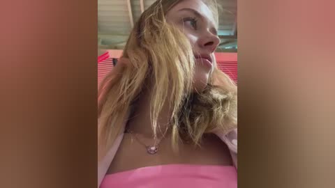 Media: Video of a young woman with long blonde hair, wearing a pink strapless top, sitting in a red car with sunlight filtering through the windows.