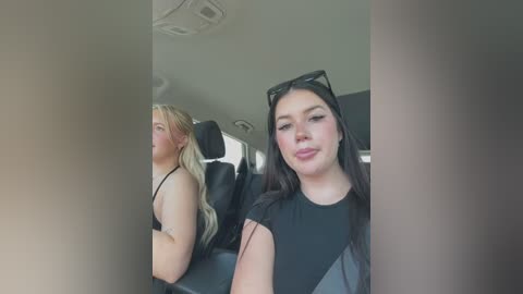 Media: Video of a blonde woman in a black top and a woman with long black hair in sunglasses, both seated in a car with dark interior.