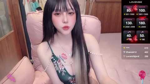 Media: Video of a pale-skinned, long-haired Asian woman with a slender build, wearing a floral top, sitting on a plush pink chair.