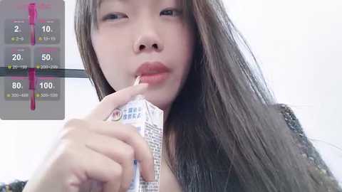 Media: Video of an Asian woman with long brown hair, holding a condom packet, in a close-up. Background shows a digital thermometer graph.