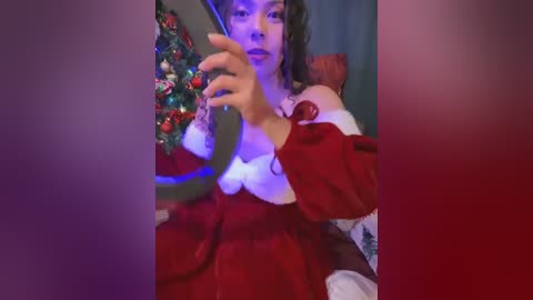 Media: Video of a young woman in a red velvet Santa dress, holding a smartphone, against a festive backdrop with a Christmas tree and decorations.