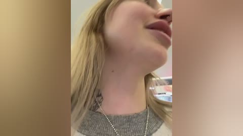 Media: Video of a close-up side profile of a young woman with fair skin, straight blonde hair, and a silver necklace, viewed from the neck up.