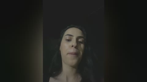 Video of a woman with long, dark hair, light skin, and closed eyes, set against a dimly lit background, creating a serene, contemplative mood.