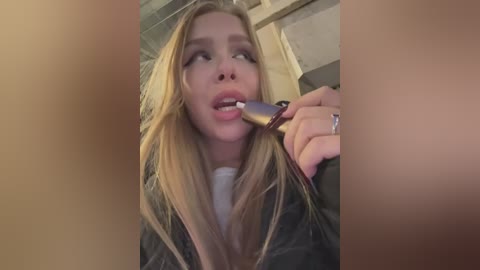 Media: A close-up video of a blonde woman with long hair, wearing a black jacket, eating a spoonful of ice cream. She appears to be in an indoor setting with a wooden background.