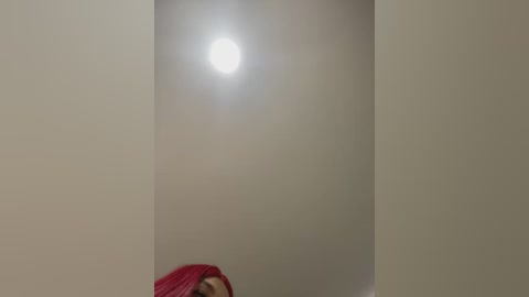 Media: Video of a ceiling light emitting a bright, circular glow against a plain, off-white wall, with a hint of red fabric visible at the bottom.