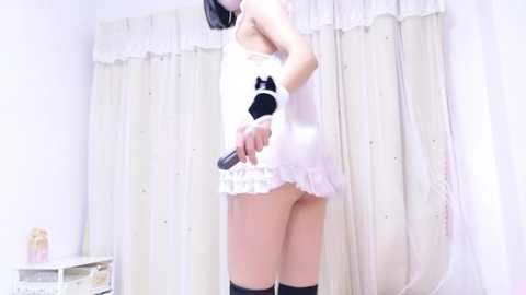 Media: Video of an Asian woman in white lingerie and thigh-high stockings, holding a black microphone, facing a white curtain backdrop.