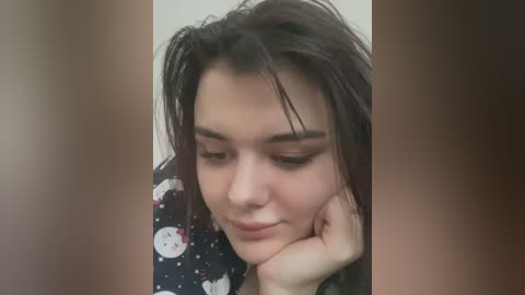 Media: Video of a young woman with shoulder-length dark hair, resting her chin on her hand, wearing a black and white patterned blouse.