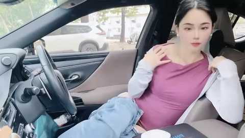 Media: Video of a pregnant East Asian woman in a car, wearing a purple top and jeans, seated next to a man in a white jacket.