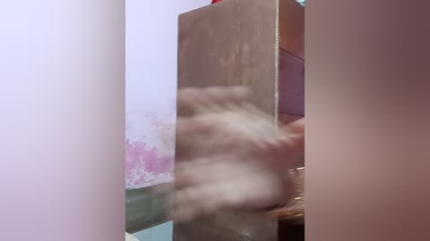 Media: A blurry video of a person's arm and hand, possibly reaching for something, with a textured, beige wall and a partially visible purple-painted wall in the background.