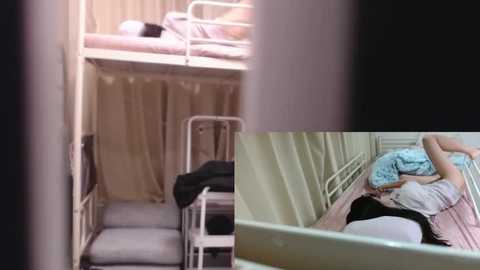 Media: Video of a cramped bunk bed room with beige curtains, white metal frames, and a messy bed with a blue blanket, showing a distressed young woman in a blue shirt, sitting on the lower bunk, her face in her hands.