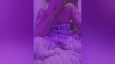 Media: Video of a topless woman with tattoos and light skin, covered in a fluffy white substance, holding a sign that says \"AMAZING.\" Background is purple.