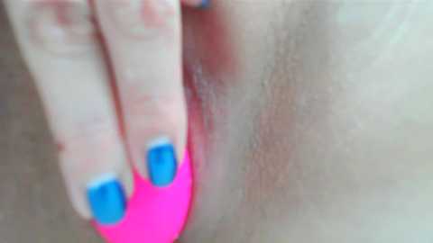 Media: Close-up video of a person's hand with bright blue nail polish pressing a pink vibrator against their vulva. The image is intimate and explicit, focusing on the genital area.