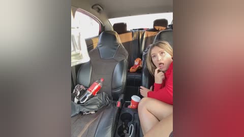 Media: Video of a blonde woman in a red sweater, eating a snack, sitting in the back seat of a car, with open food containers and drinks on the seat.