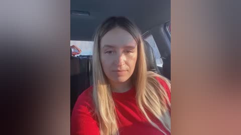 Media: Video of a young woman with long blonde hair, fair skin, and a red shirt, sitting in a car; blurry background.