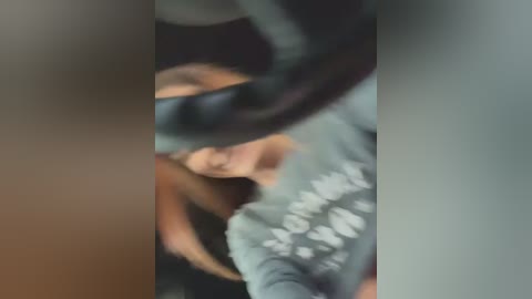 Media: Blurry video of a woman with light skin and long brown hair, wearing a grey sweatshirt with white text, possibly dancing or moving. Background is dark and out of focus.