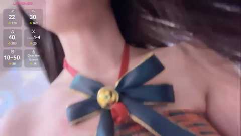 Media: Video of a woman with light skin, wearing a red strapless top adorned with a large, multi-colored, star-shaped brooch featuring gold accents. Background is blurred, showing a room with a bed.