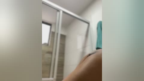 Media: A blurry video of a person's back in a modern bathroom with a teal towel and beige tiles.