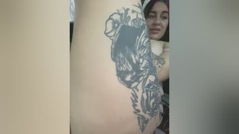 Media: Video of a woman with long brown hair, wearing a red top, showing off a large, detailed tattoo of a bat on her left thigh.