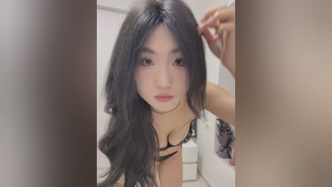 Media: A video of an Asian woman with long, wavy black hair, fair skin, and full lips, wearing a black lace bra. She is adjusting her hair in a white bathroom.