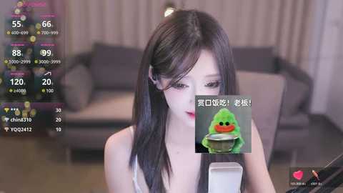 Media: A video of an East Asian woman with long black hair, wearing a white tank top, in a modern living room with a gray sofa. Overlayed are live streaming stats and a green slime character.