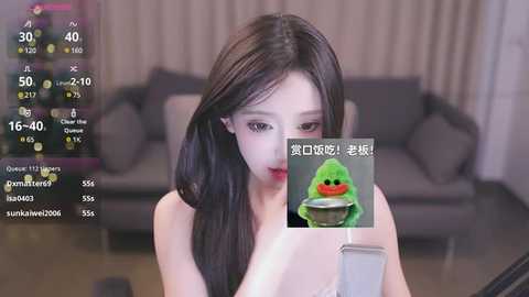 Media: A video of an Asian woman with long black hair, light skin, and a slim figure, wearing a green hoodie, holding a green plush toy, in a modern living room.