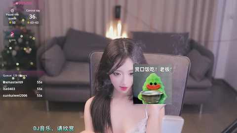 Media: Video of an Asian woman with long black hair, wearing a light-colored lace bra, seated at a table in a modern living room.